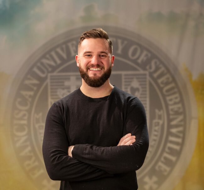 Portrait of John Paul Von Arx standing in front of the Franciscan University of Steubenville seal.