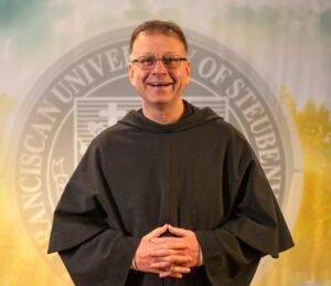 Fr. Shawn Roberson, T.O.R., standing in front of a university seal.