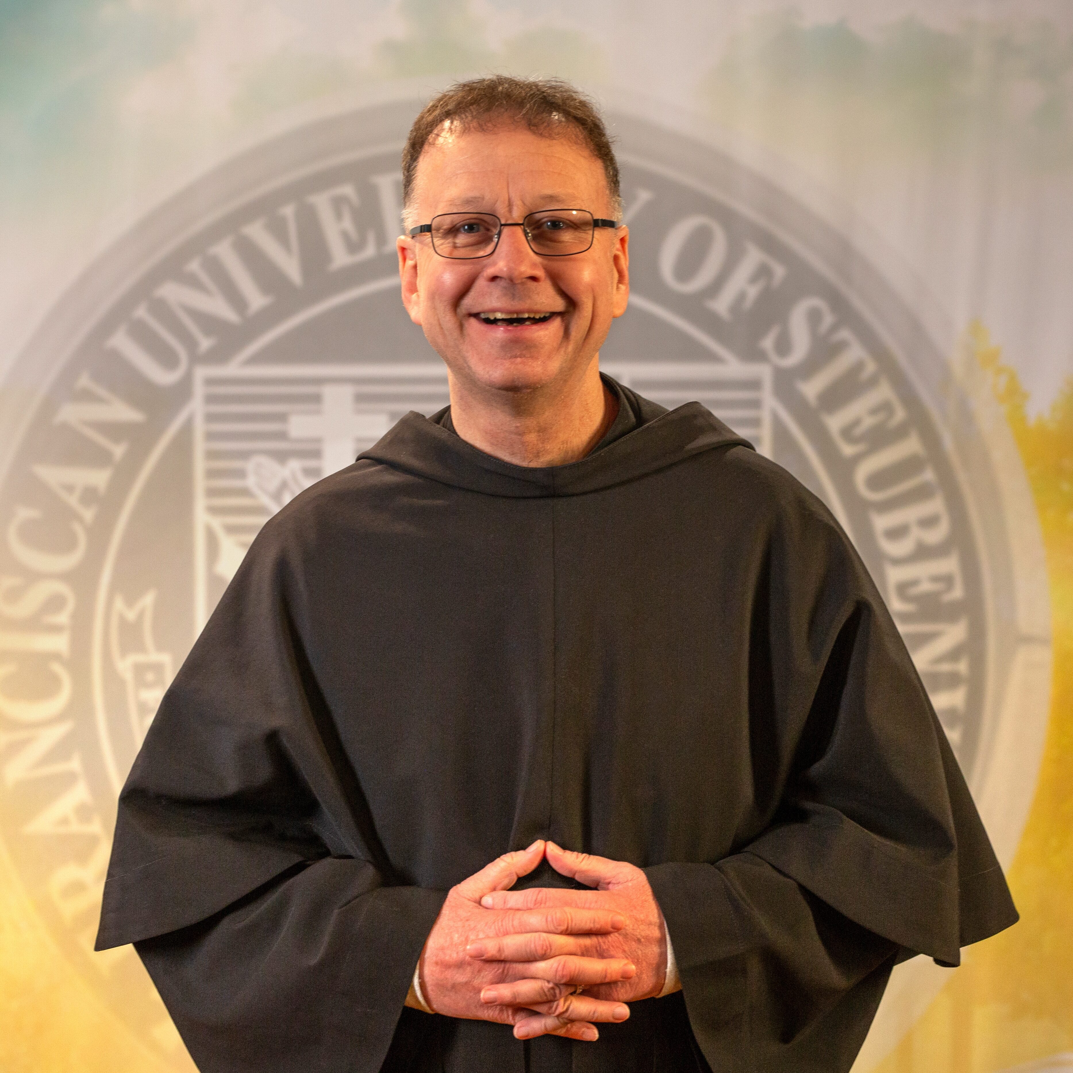 Fr. Shawn Roberson, T.O.R., standing in front of a university seal.