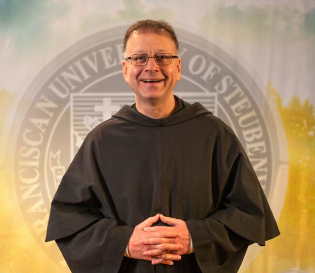 Fr. Shawn Roberson, T.O.R., standing in front of a university seal.